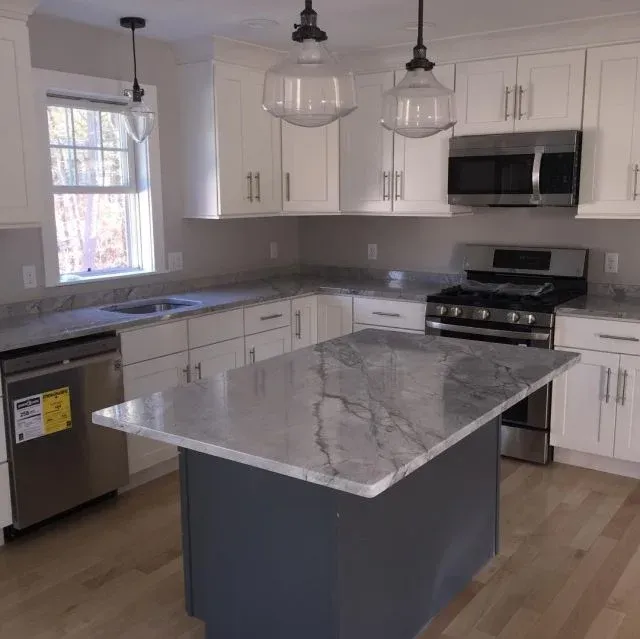 White kitchen with light grey quartzite island and glass pendants