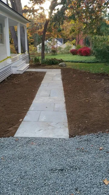 Front walkway of gray pavers leading through a newly landscaped yard beside a house