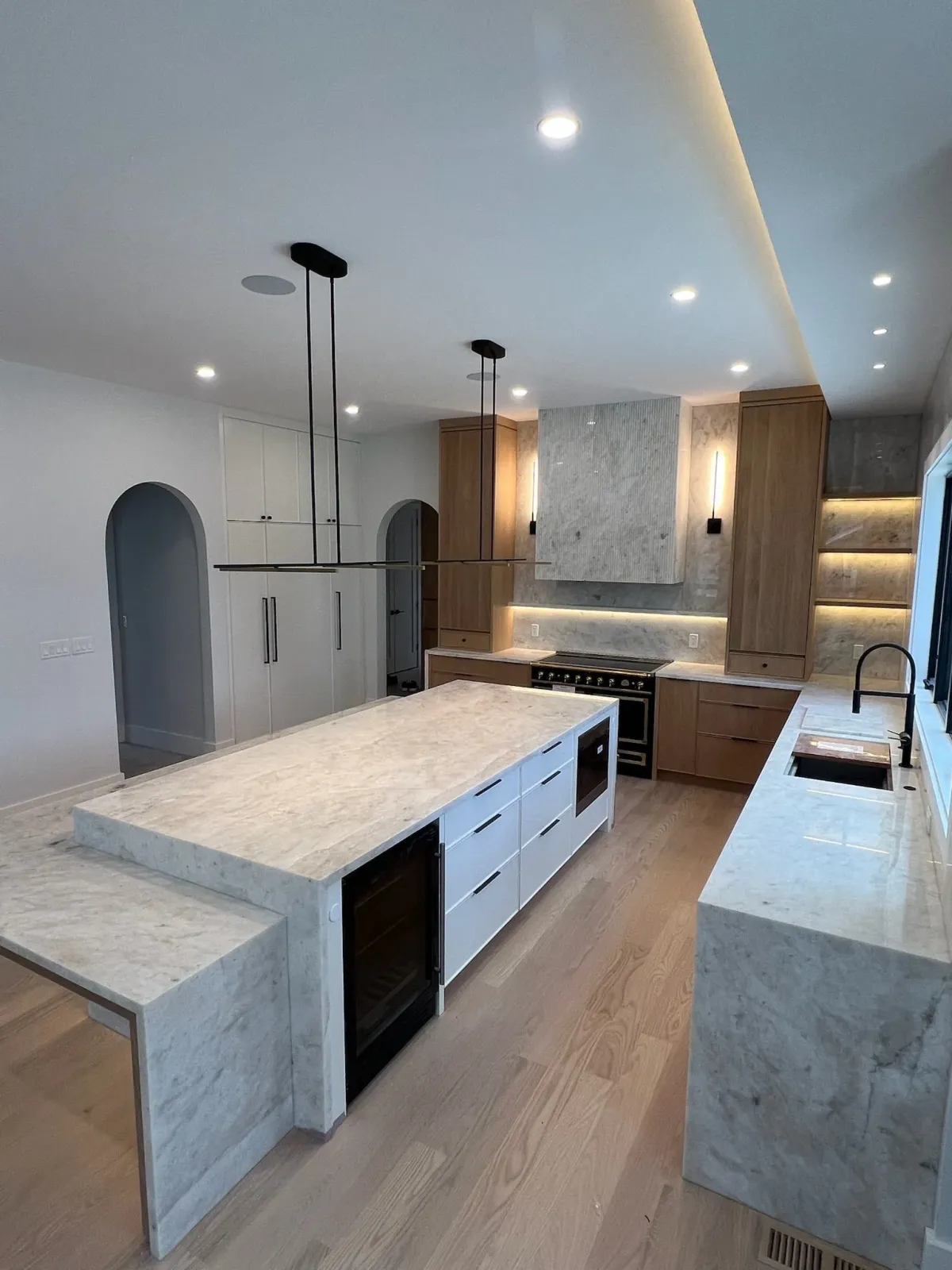 Modern kitchen with white and wooden cabinets, marble island, built-in appliances, and recessed lighting.