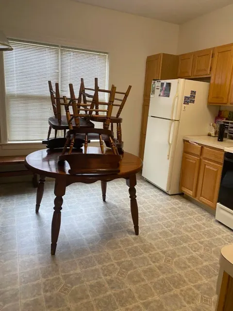 Peaceful cleanings cleaned Kitchen with wooden table and chairs stacked, white refrigerator, wooden cabinets, and tiled floor.