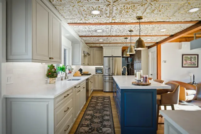 Modern kitchen design featuring gray and navy cabinets, marble countertops, decorative ceiling, and stainless steel appliances, highlighting a recent transformation by Bradford Construction Management.