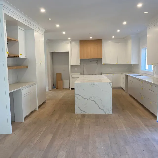 Bright modern kitchen with white cabinets, wood floors, and a marble island.