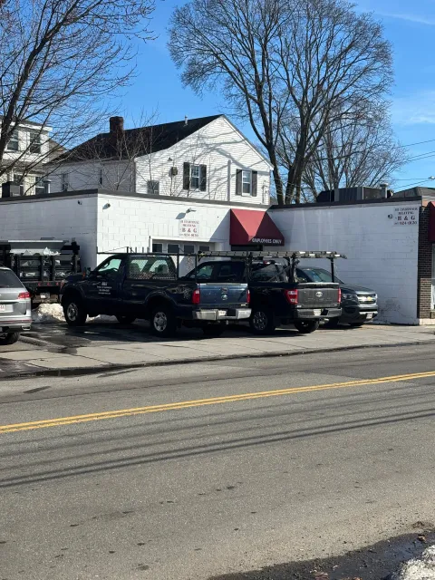 A white building with a red awning under clear blue skies, with several work trucks parked in the lot out front.
