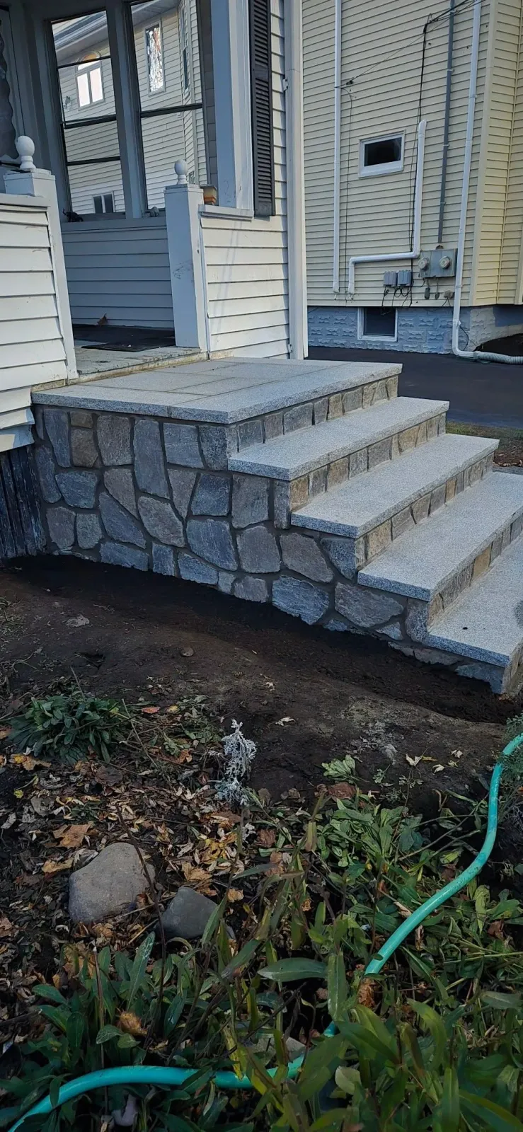 Stone steps leading to a house entrance, with surrounding earth and vegetation.