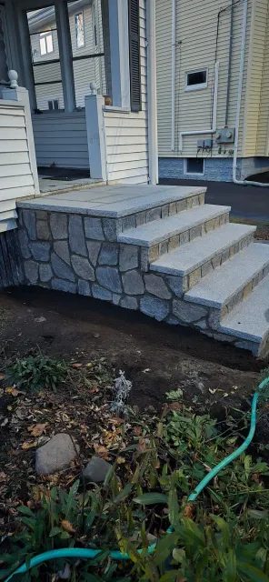 Stone steps leading to a house entrance, with surrounding earth and vegetation.