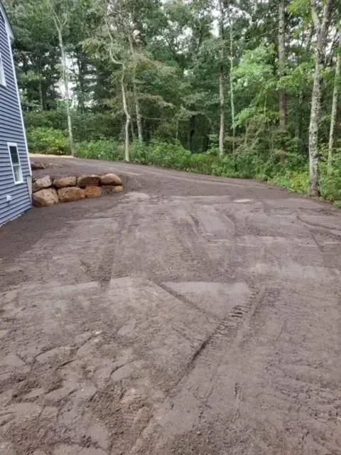 Gravel driveway beside a house, bordered by rocks and dense green trees.