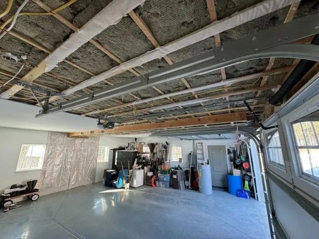 Garage interior with unfinished ceiling, concrete floor, and stored tools and supplies against the back wall