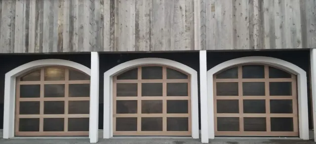 Three arched windows with white trim on a weathered wooden building facade.