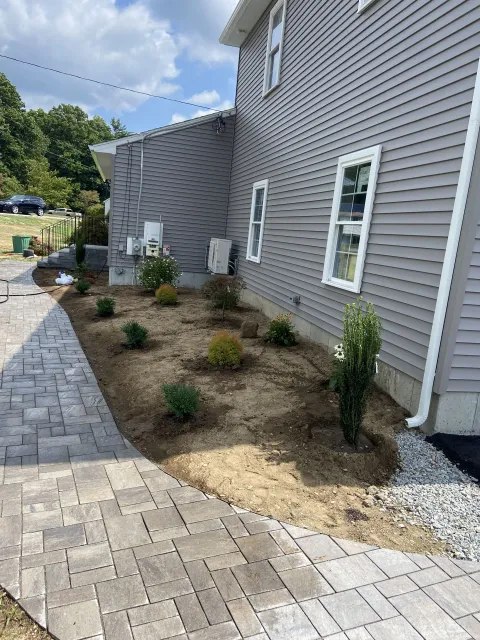 Side view of a house with new landscaping and a brick pathway.