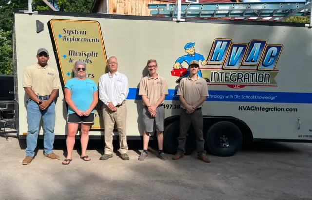Five people stand beside a HvAC Integration service truck in bright sunlight.