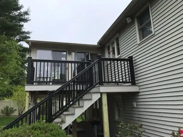 A white house with a black deck and stairs leading up to it.