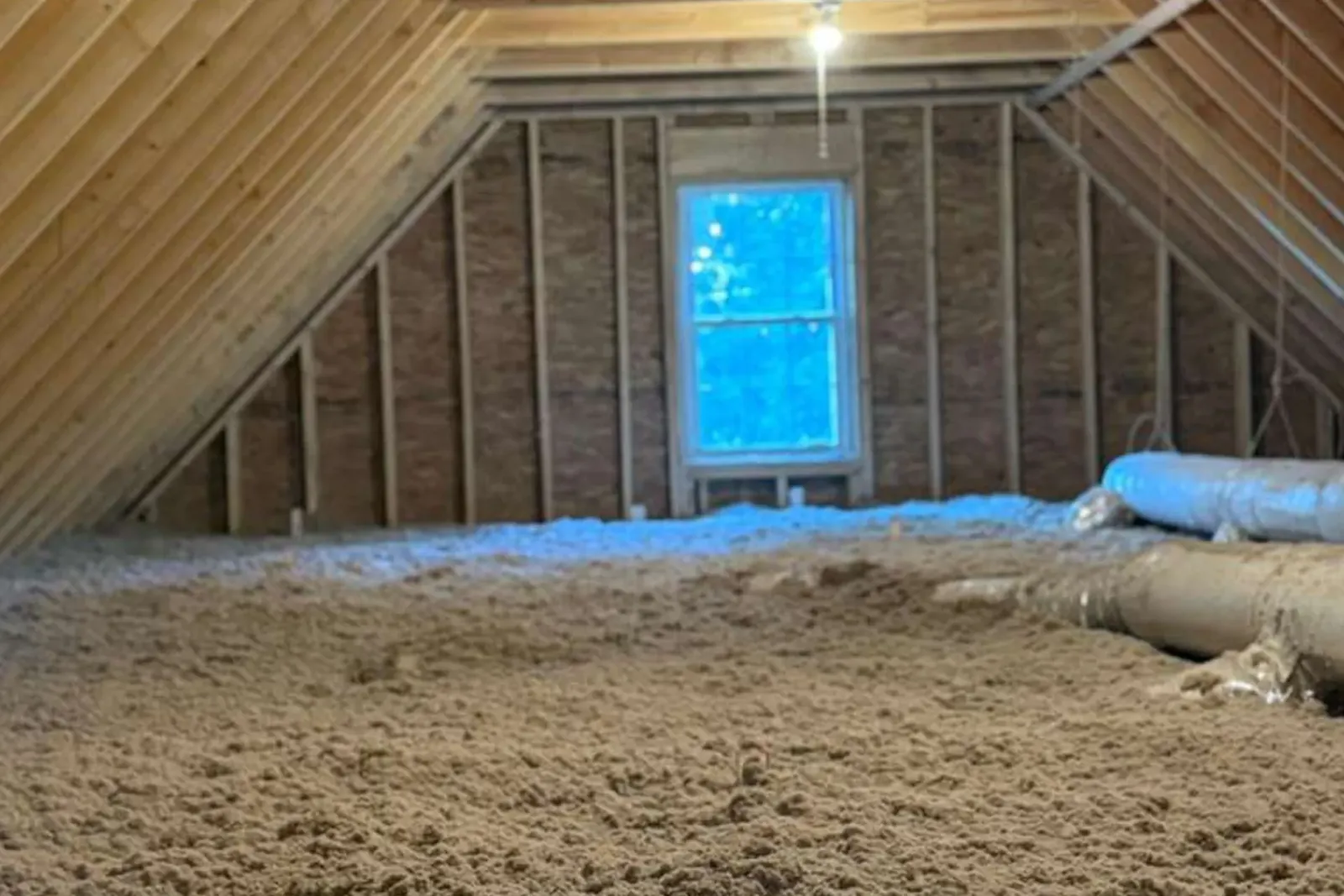 Attic interior with cellulose insulation. Wooden beams and a window are visible.