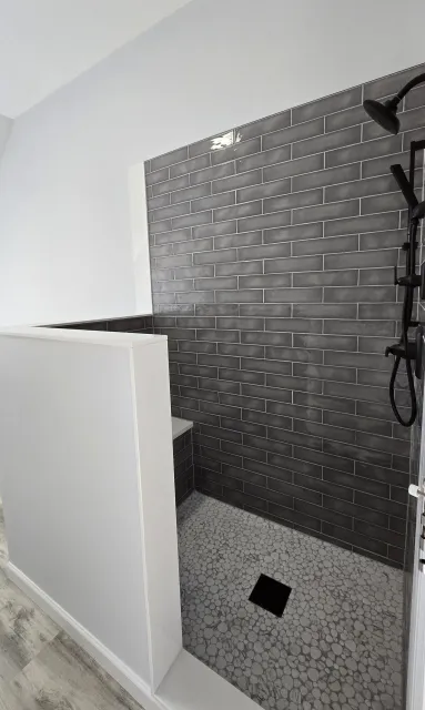 Walk-in shower with charcoal subway tile, a half wall and a pebble-style floor