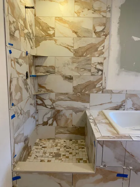 Partially tiled bathroom shower with beige stone-pattern tiles and a white bathtub edge