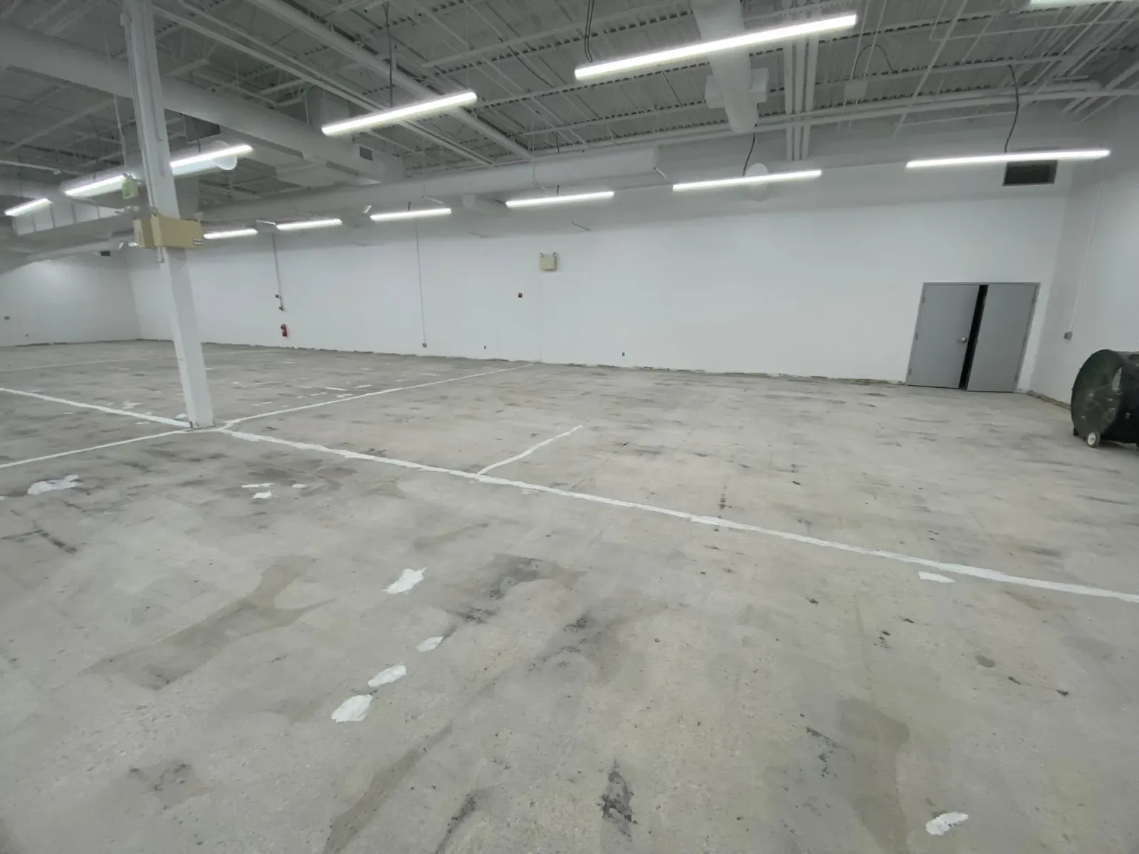 Empty industrial warehouse with white walls, concrete floor, and overhead fluorescent lights