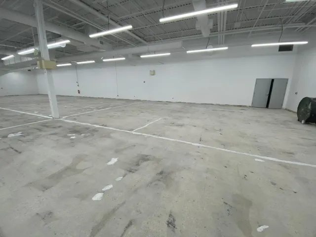 Empty industrial warehouse with white walls, concrete floor, and overhead fluorescent lights