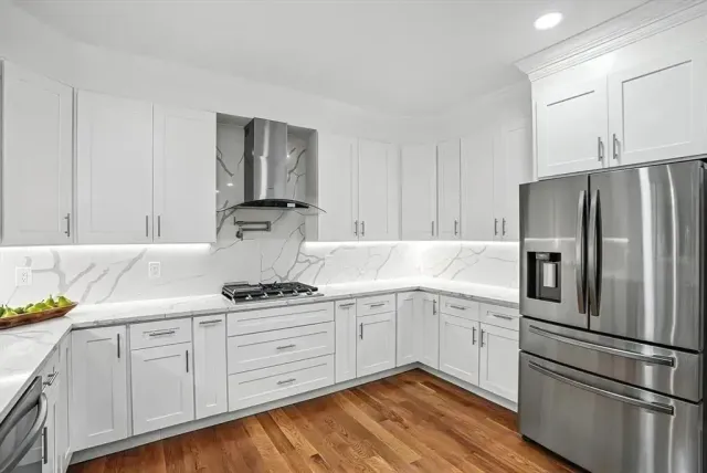 White kitchen with stainless steel appliances, marble countertops, and hardwood floors.