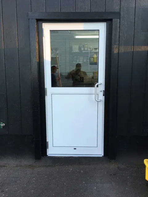 White and glass door set in a black frame, on a dark building exterior.