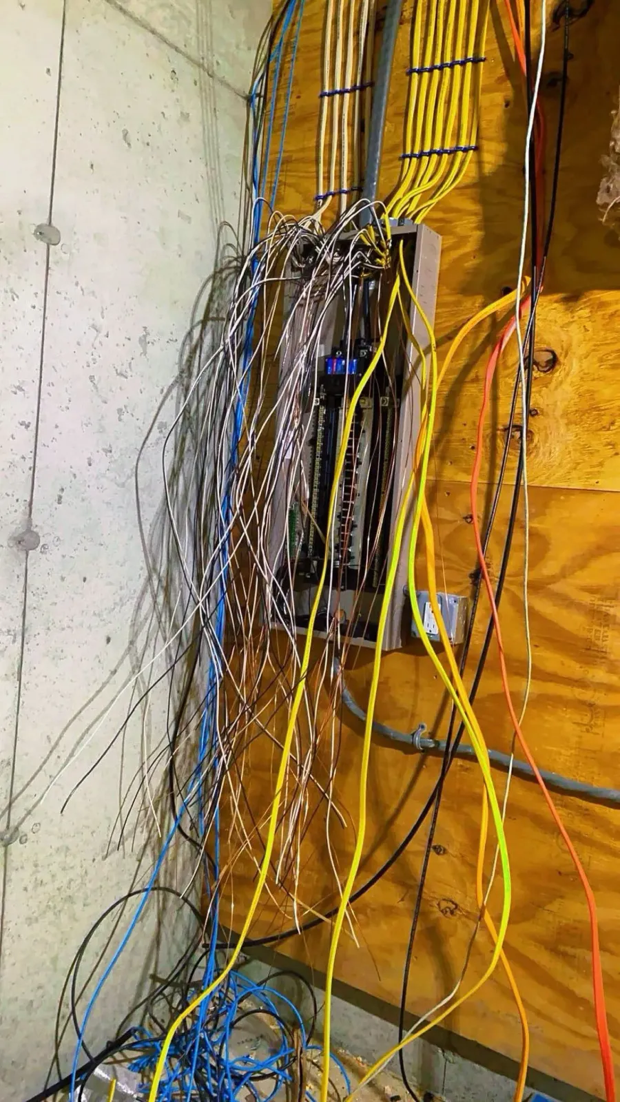 Tangled bundle of multicolored wires hanging against a wall in a cluttered utility area