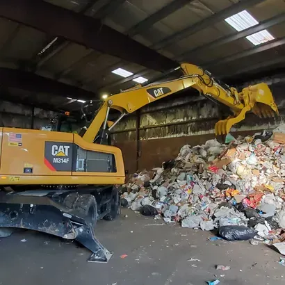 Yellow CAT excavator scoops debris inside a recycling facility.
