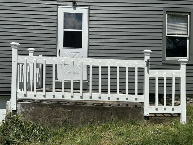 A white fence is in front of a gray house.