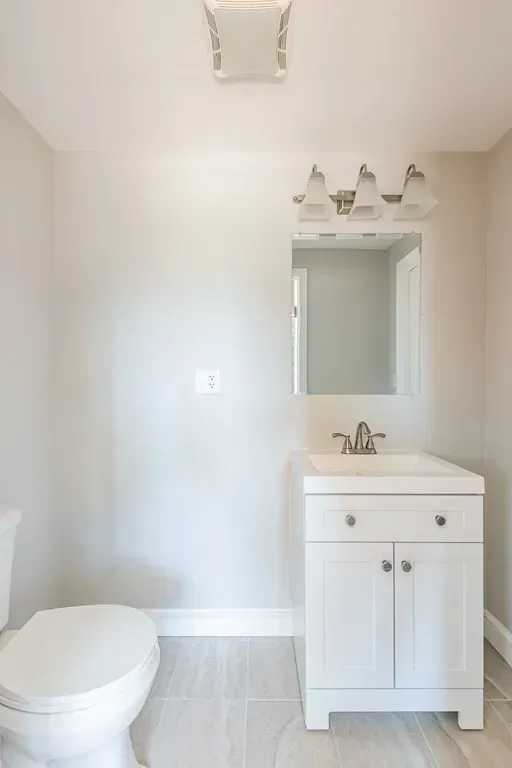 A bathroom with a toilet , sink and mirror.