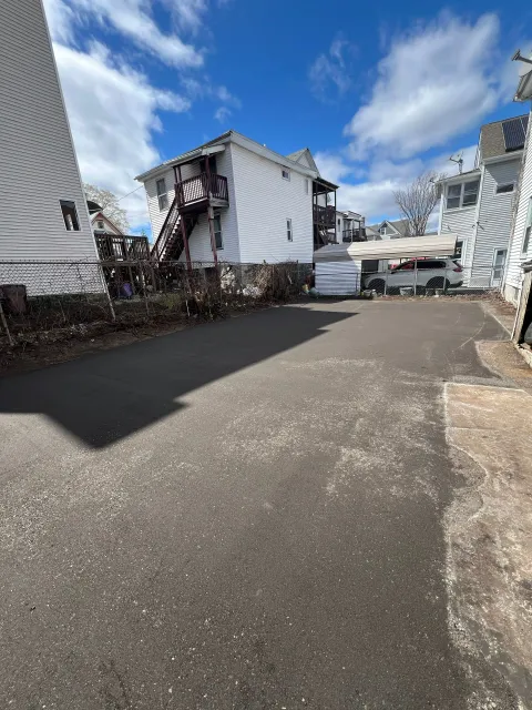 Asphalt driveway next to white buildings, a blue sky with clouds overhead.