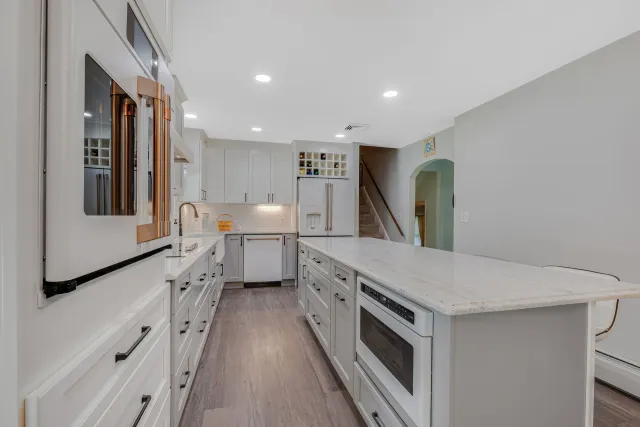 A kitchen with white cabinets, granite counter tops, stainless steel appliances and a large island