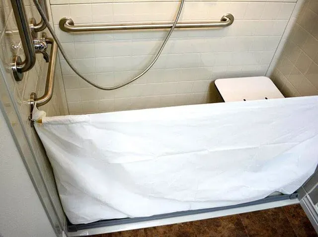 White shower bench in a tiled bathroom with metal grab bars and a folded shower curtain.