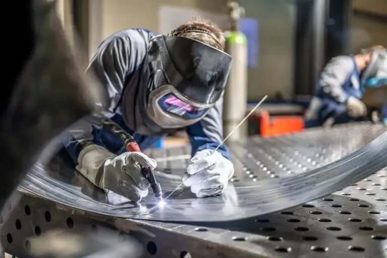 Welder in full protective gear welding a curved metal sheet, sparks flying.