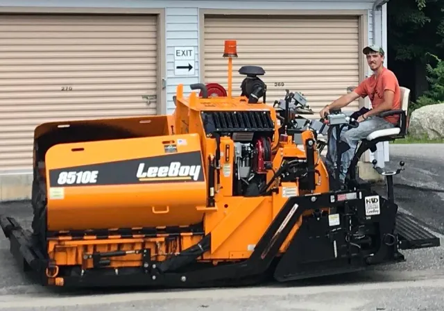 A man is driving a asphalt paving machine.