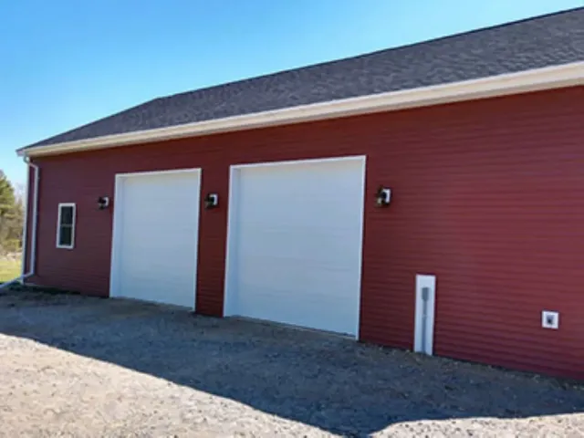 A red garage with two white garage doors and a blue sky in the background.