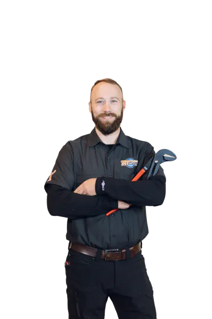 A smiling man with a beard and short hair, wearing a black uniform with a logo on the chest, holding a pipe wrench with his arms crossed.