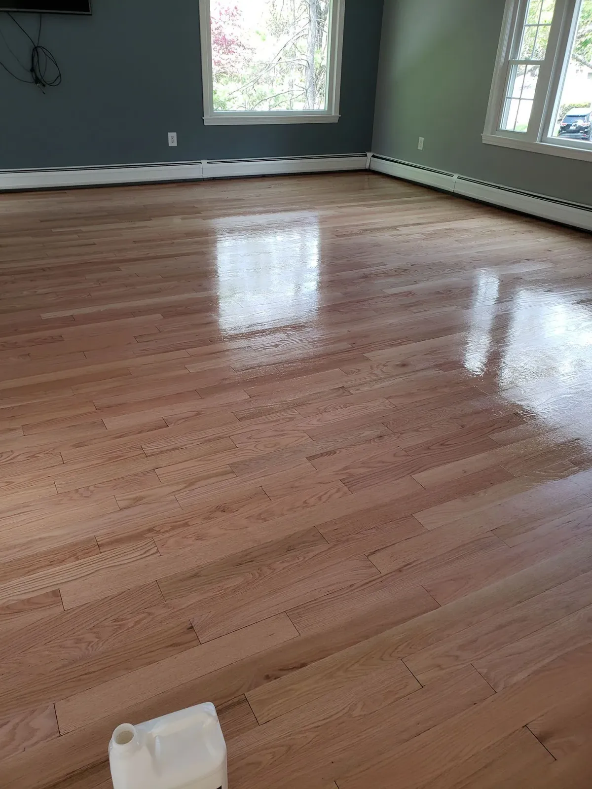 A large wooden floor in a living room with a bottle of polish on it