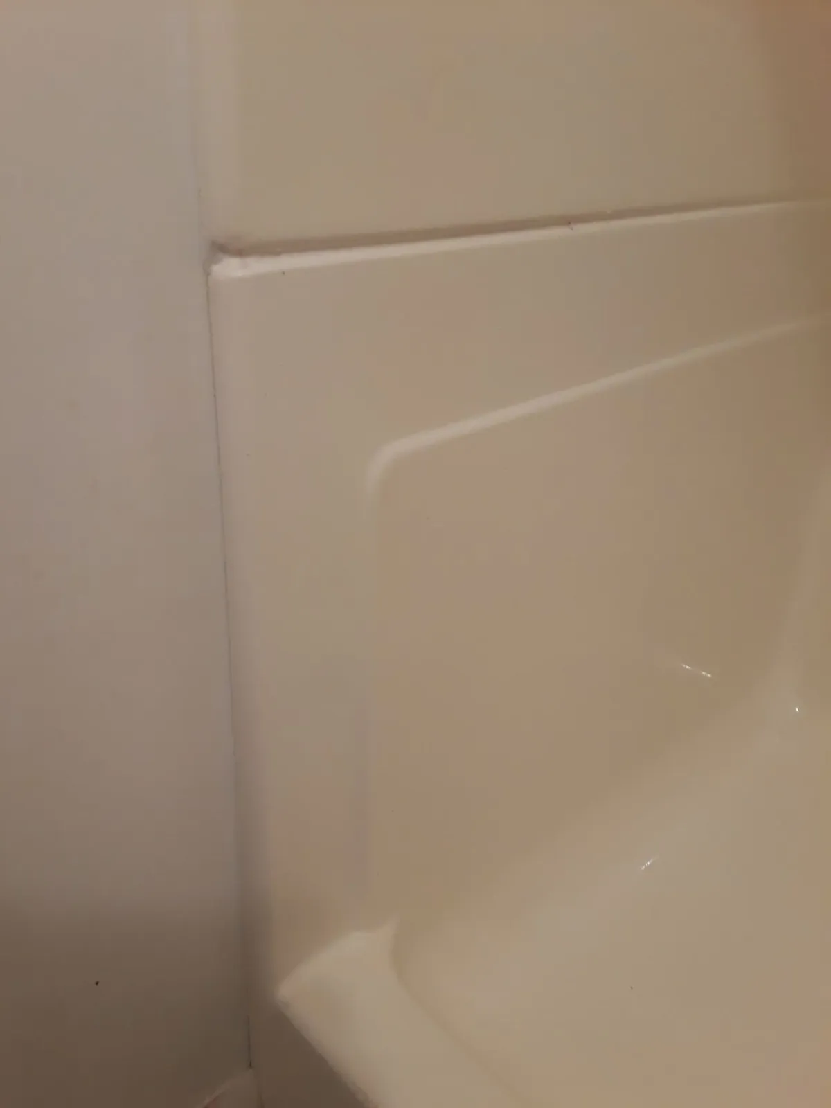 Cream-colored shower wall with a ledge, next to a white wall.