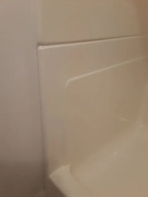 Cream-colored shower wall with a ledge, next to a white wall.