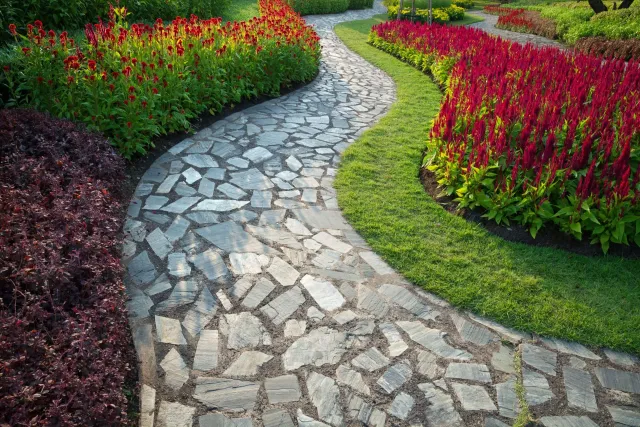 Stone path curves through a garden with red and green flowers.