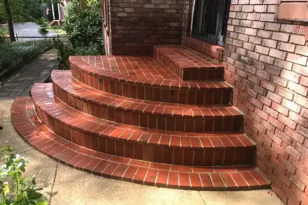 After: Curved brick staircase with multiple steps leading up to a door, surrounded by greenery and a brick wall.