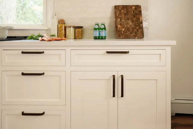 Kitchen counter with jars of pasta and a cutting board, with a window showing greenery outside.