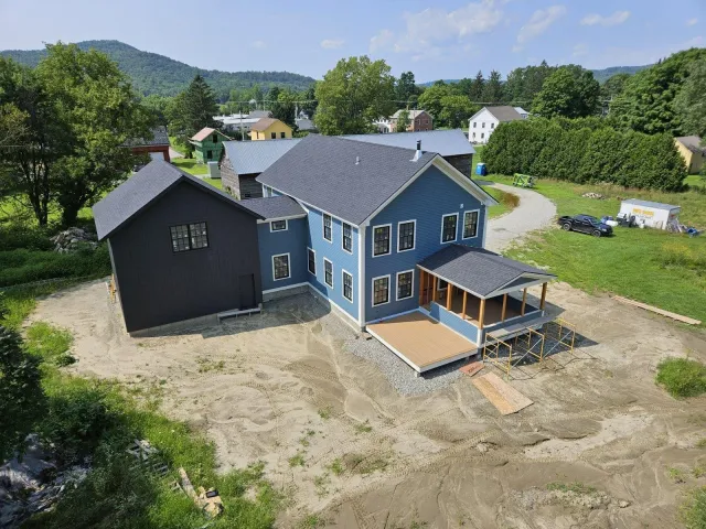 Large blue home and black attached garage on a rural neighborhood road, photographed from above.