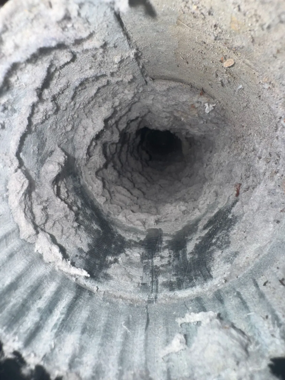 Inside a dryer duct caked with a thick felted layer of lint, leaving an opening a fraction of the duct’s full diameter.