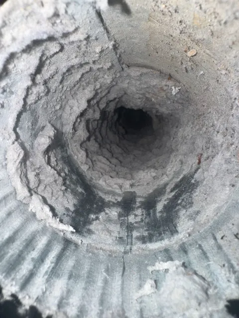 Inside a dryer duct caked with a thick felted layer of lint, leaving an opening a fraction of the duct’s full diameter.