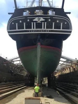 A low-angle rear view of the USS Constitution's hull in dry dock, showing its green-painted bottom and rudder.