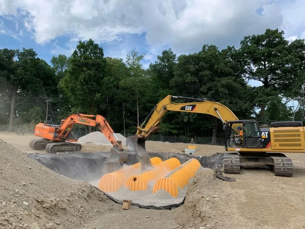 Two excavators work to cover underground utilities  with dirt on a site development project.
