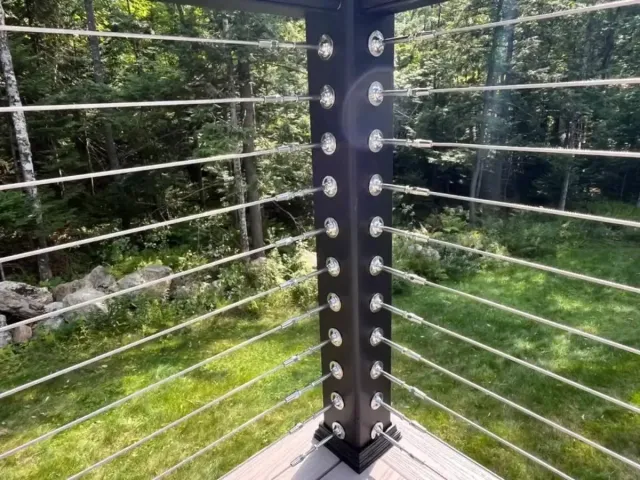 Metal railing corner with horizontal cables overlooking a green wooded area