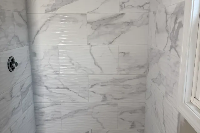 Finished marble-look tub-shower surround with white wave-textured wall tile, installed by Dmtilellc in Newington, CT