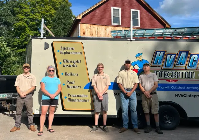 HVAC technician team posing beside a service truck and a signboard outside a house