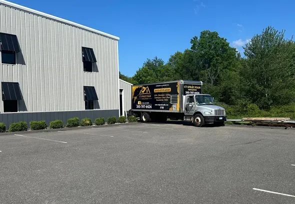 Truck parked outside a building. Building has wavy silver siding and black window awnings. Sunny day.