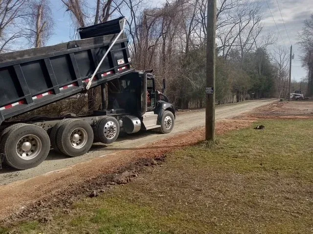 Dump truck unloading gravel on rural dirt road