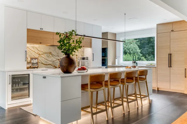 Modern Marshfield kitchen remodel with white high-gloss cabinets, quartz island, leather stools, and a gold-veined granite slab backsplash